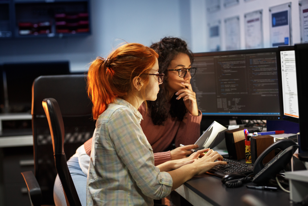 two women in dark room in front of computer screens, programmers, coders