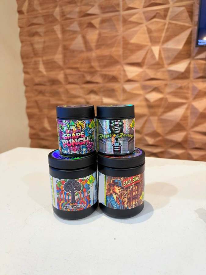 Stacked black Washington cannabis jars on a counter in front of a cedar paneled wall at Origins
