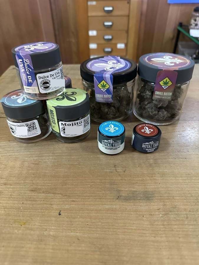 Small batch cannabis jars and limited batch tins lined up on a wooden counter at Origins